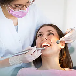 A patient having her teeth cleaned by a helpful and friendly dental hygienist. The dental hygienist is wearing a face mask and gloves to ensure a safe and cleanly experience.