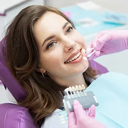 A patient sitting in a dental chair while a dental professional matches up veneers to her natural smile.